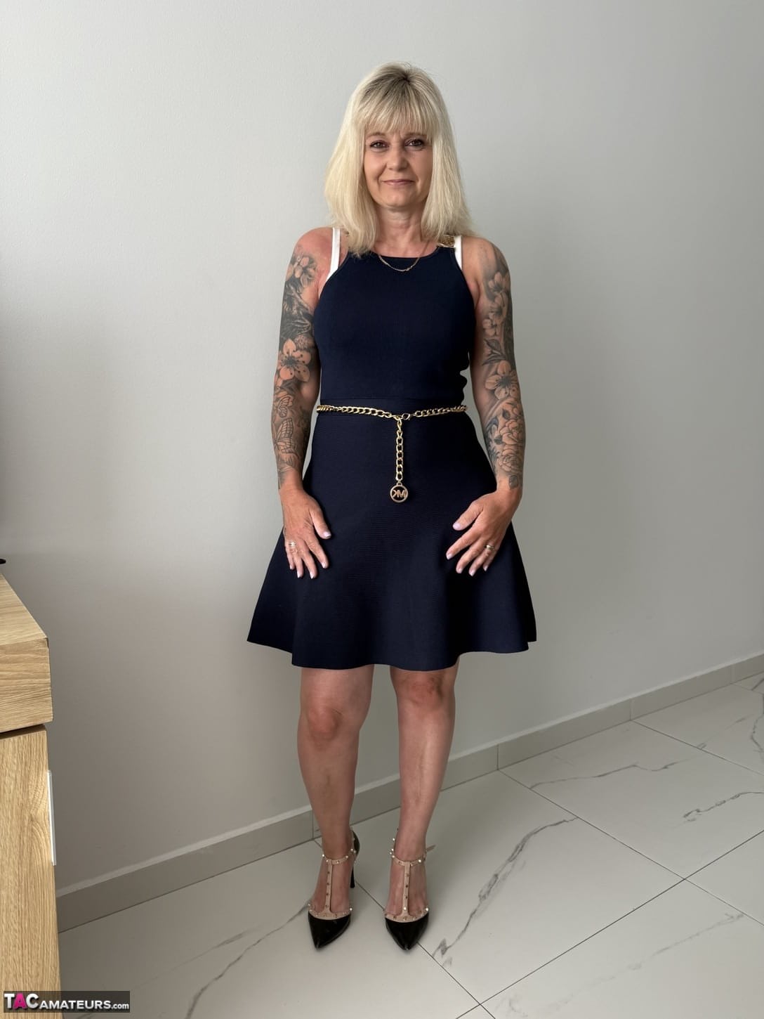 Tattooed older blonde unzips from a dress to get naked in high heels