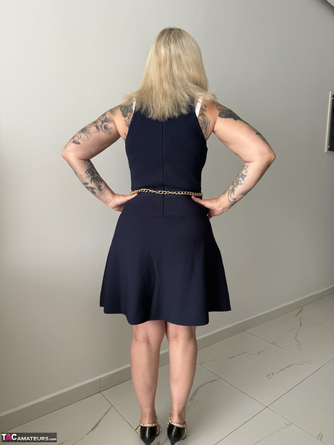 Tattooed older blonde unzips from a dress to get naked in high heels