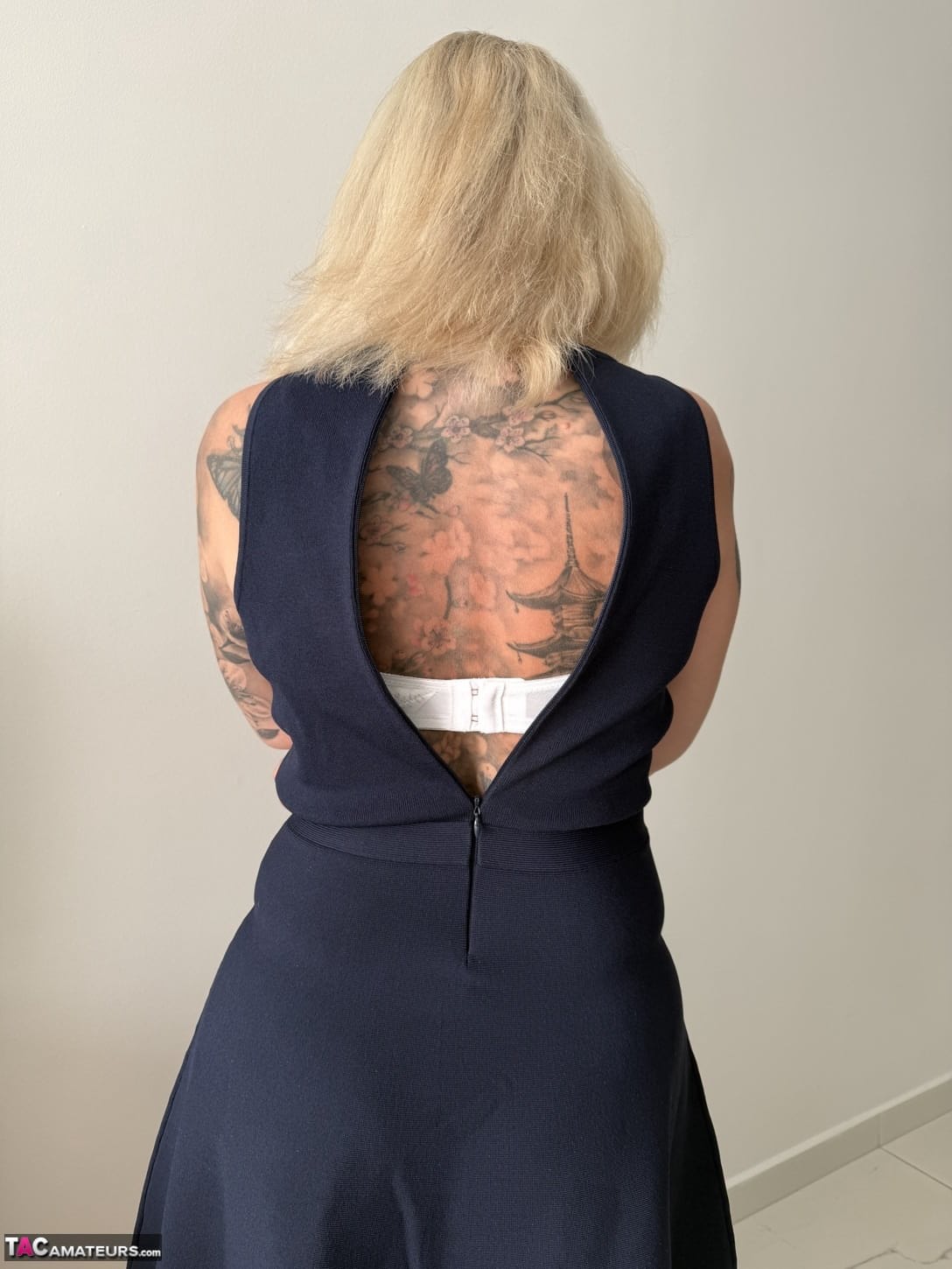 Tattooed older blonde unzips from a dress to get naked in high heels
