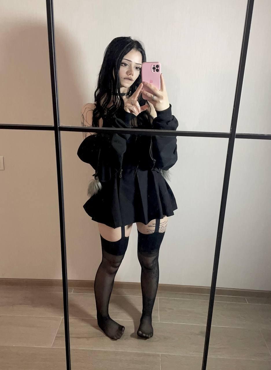 Dark-haired girl takes selfies while wearing black stockings and a black dress